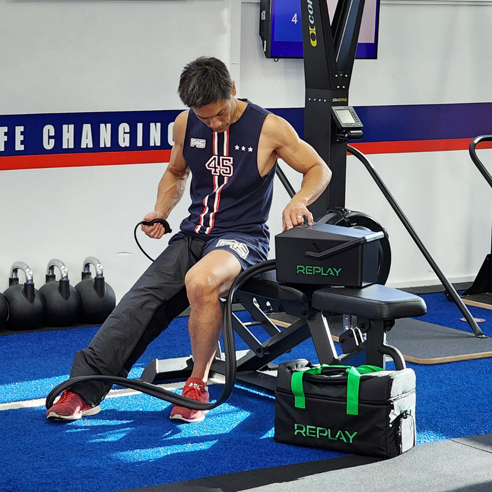 Athlete using Replay Pro ice compression leg wrap with air pump for recovery in gym setting