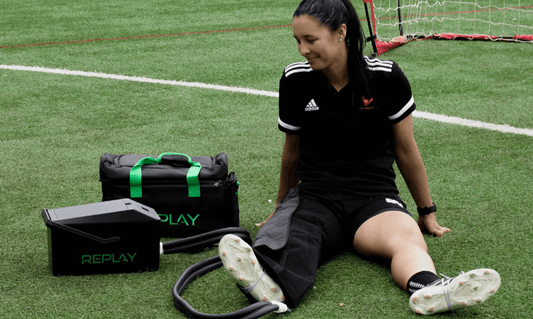 Athlete sitting on a sports field using a Replay Pro ice compression unit for knee recovery after training, showing the benefits of cold and compression therapy.