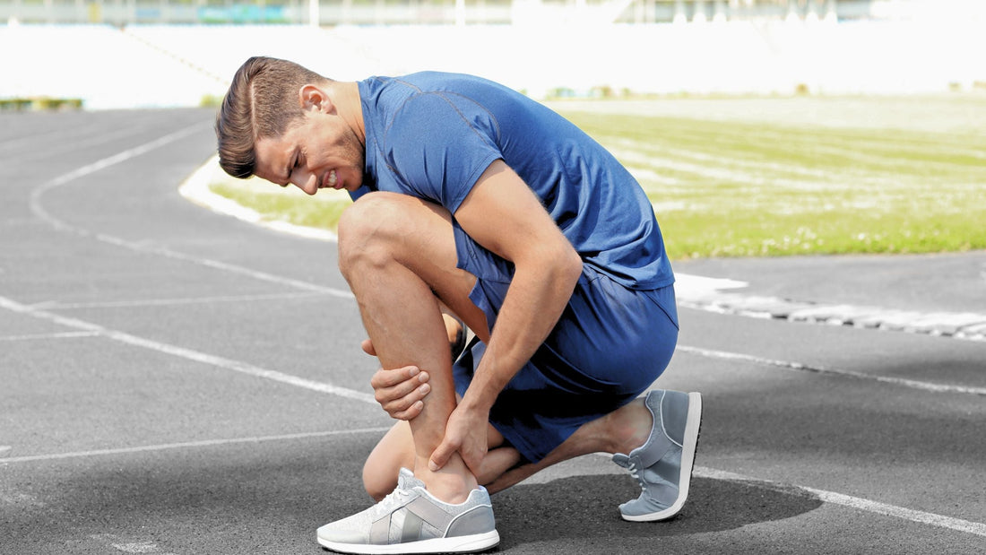 Runner crouching on a track holding his knee, showing muscle soreness or possible injury after training.