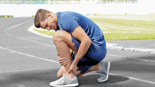 Runner crouching on a track holding his knee, showing muscle soreness or possible injury after training.